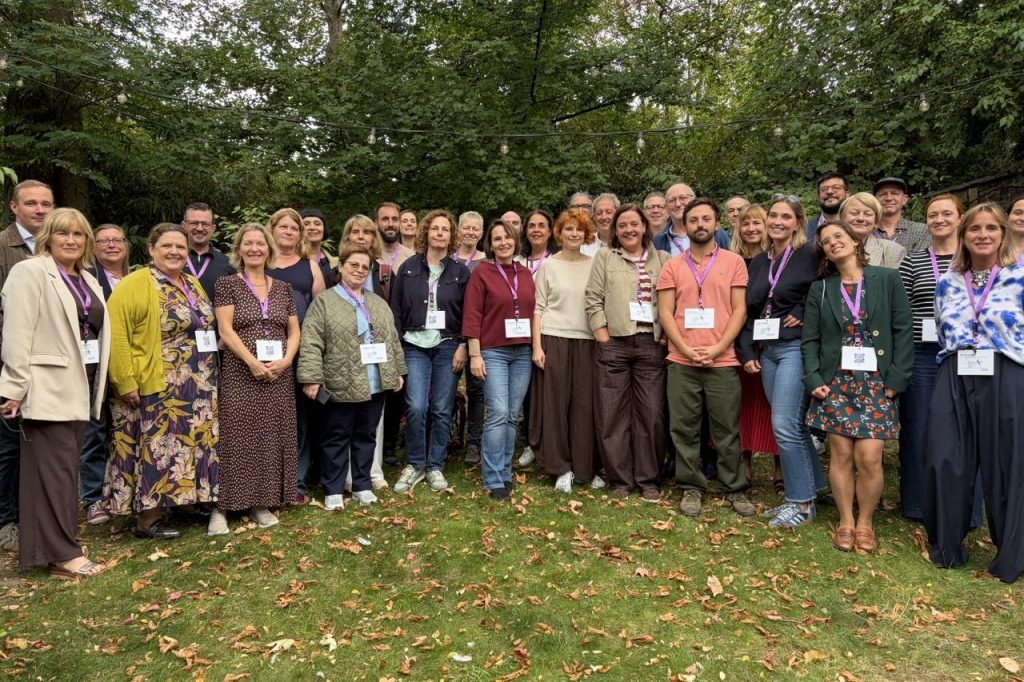 Participants of the ASEE General Assembly pose together in a garden, wearing purple lanyards, on grass covered with autumn leaves (Brussels, 29-30 September 2026).